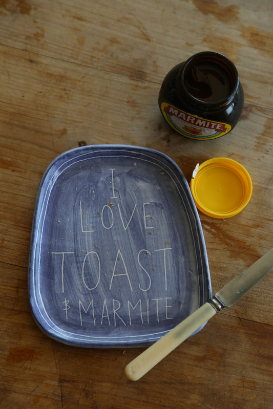 A handmade stoneware plate with the words 'I LOVE TOAST & MARMITE' written in the center, accompanied by a jar of marmite